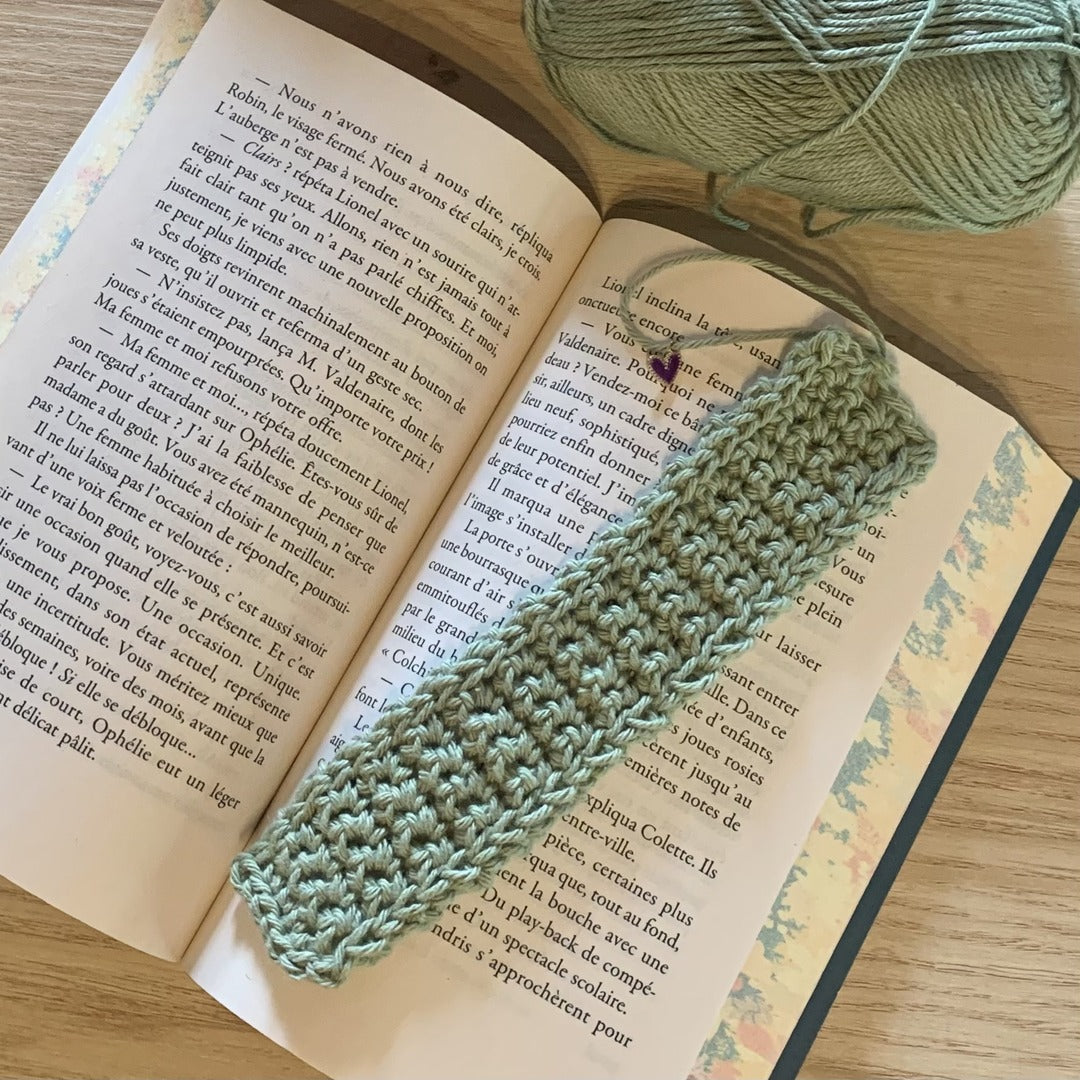 Marque-page vert sauge réalisé au crochet posé sur un livre ouvert